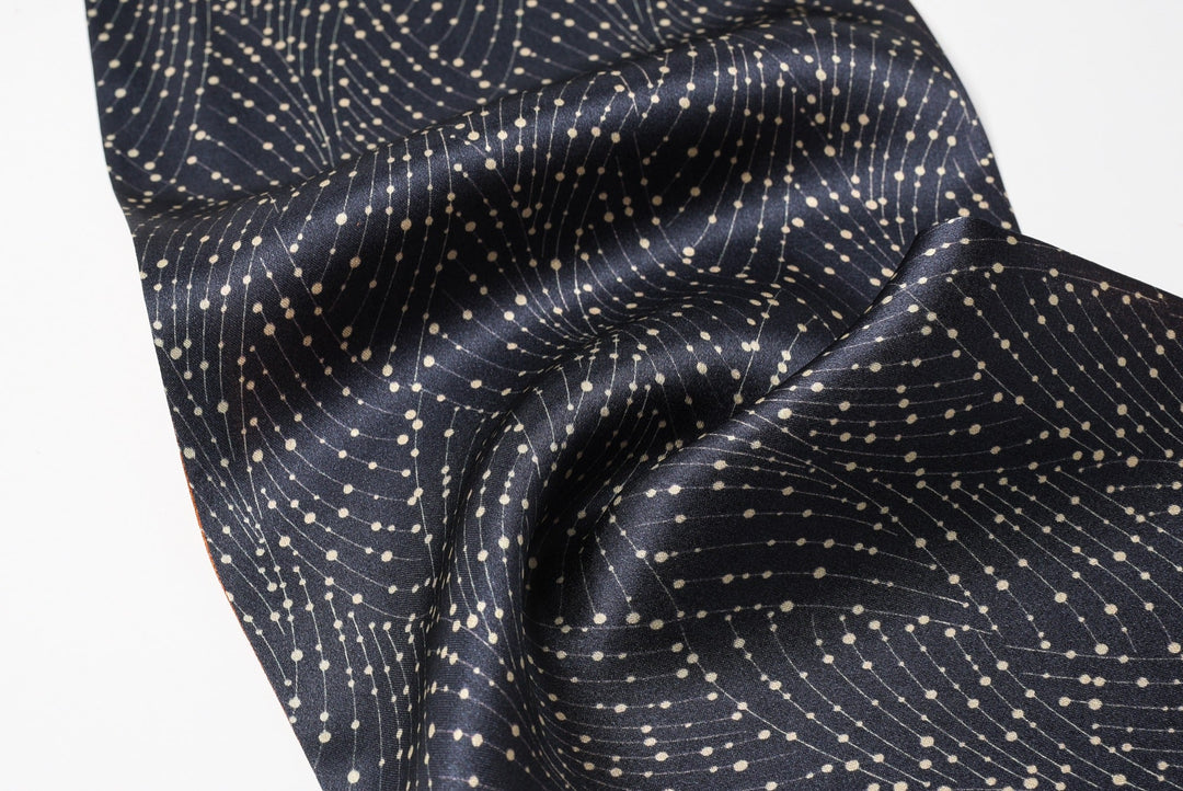 A close-up of the SusanSilk Orange Flower Sprigs Silk Long Fluttering Belt, showcasing its silky smooth texture with a dark blue base adorned by interconnected white dots forming delicate curved lines. The fabric appears lustrous, adding an elegant touch.