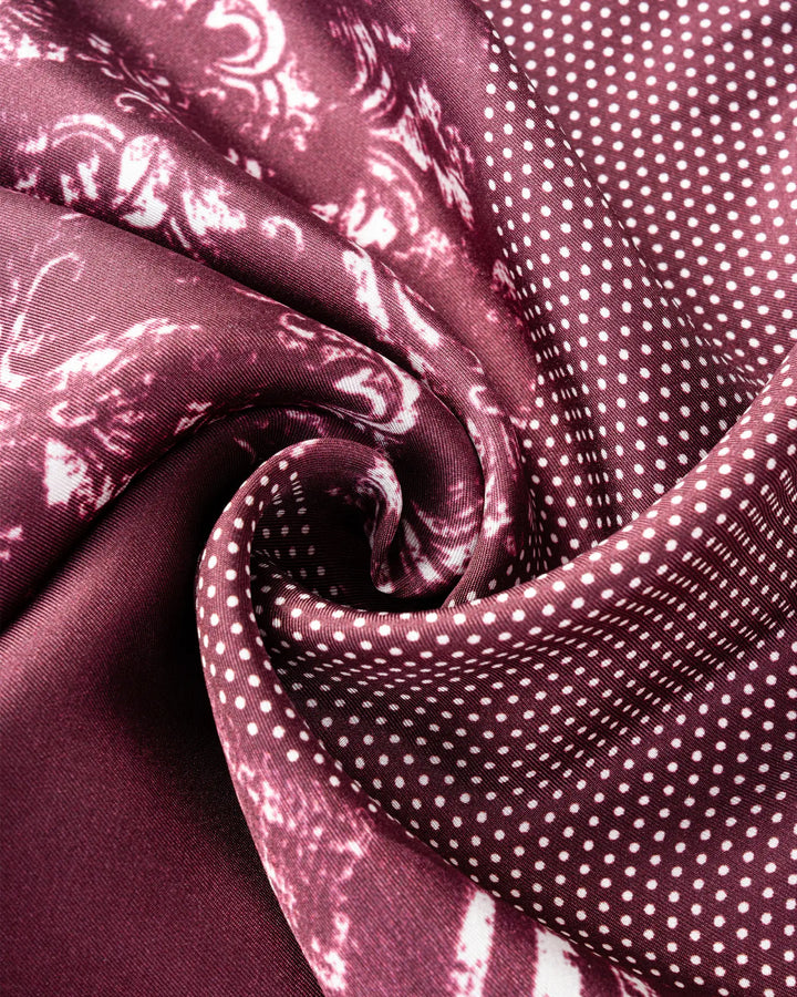 Close-up of the SusanSilk Straits Red Square Silk Scarf, showcasing its intricate patterns and white polka dots, elegantly folded and twisted to create a textured, spiral design.