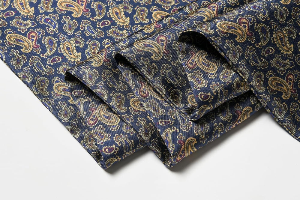 The Paisley Men's Silk Twill Scarf - Navy by SusanSilk features a folded fabric with a luxurious paisley pattern in shades of gold, red, and blue on a dark blue background.