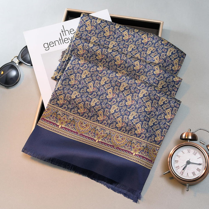 A Paisley Men's Silk Twill Scarf in navy by SusanSilk lies next to a pair of sunglasses, a magazine, and a small clock.