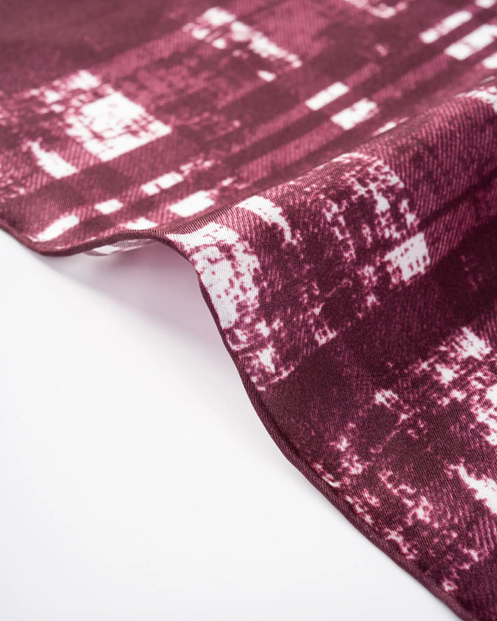 A close-up view of the Straits Red Square Silk Scarf by SusanSilk, showcasing its maroon and white textured silk fabric with an abstract pattern, gently folded on a white surface.