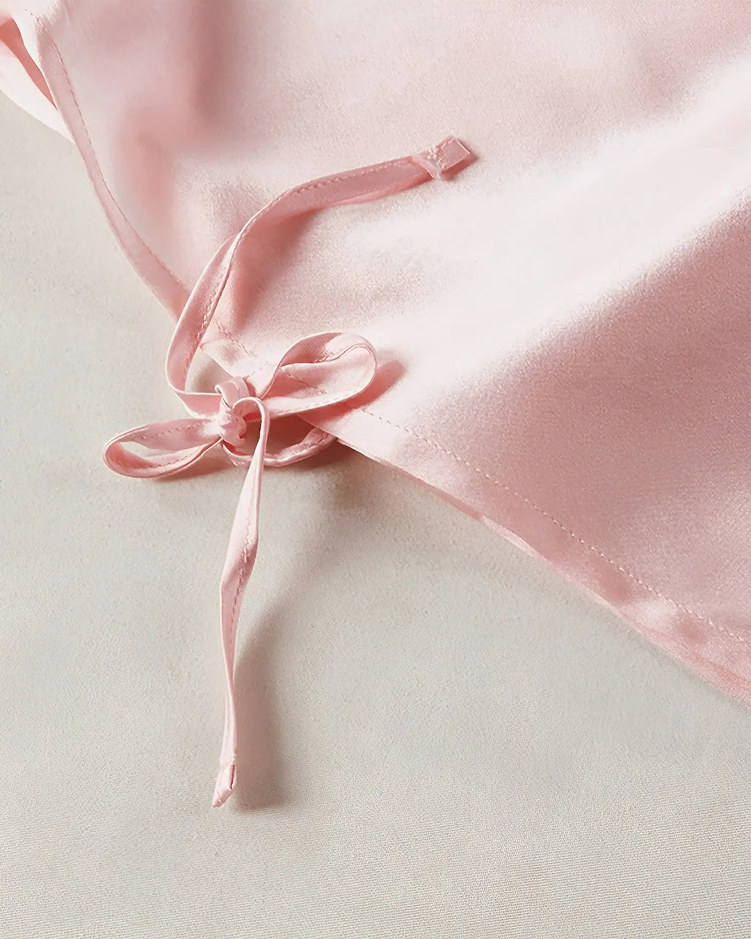 Close-up of a pink satin fabric with a tied ribbon bow, showcasing its smooth and shiny texture. This 16 Momme Antibacterial Mulberry Silk Travel Sleep Sack by SusanSilk epitomizes elegance.