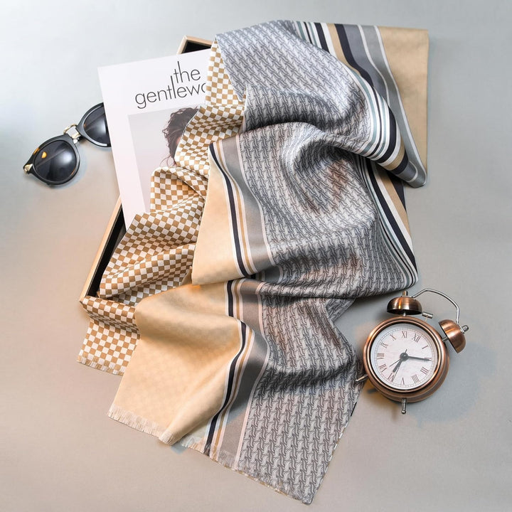 A Luxurious Men's Silk Twill Scarf in Grey Khaki by SusanSilk, an analog clock, and sunglasses are arranged on a flat surface alongside a magazine titled "The Gentlew.