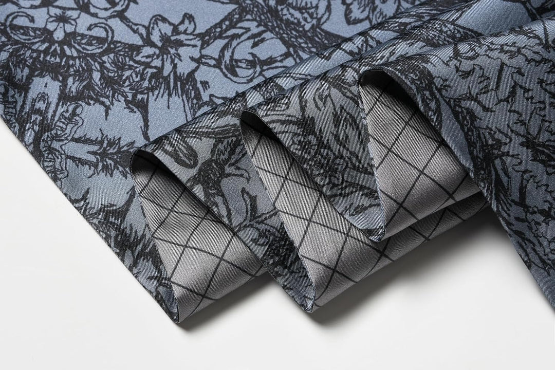 A close-up of the Luxurious Men's Silk Twill Scarf - Gentleman Gray by SusanSilk, displaying two different designs: an intricate floral pattern and a grid pattern, all in shades of gray and light blue.