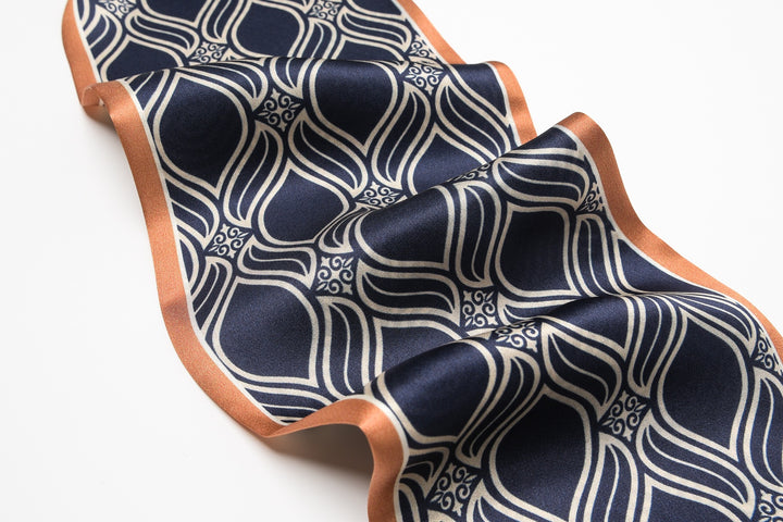 A piece of the Diamond Stripe Silk Long Fluttering Belt from SusanSilk, showcasing a navy blue and white geometric pattern with a rust-colored trim, is spread out on a light background.