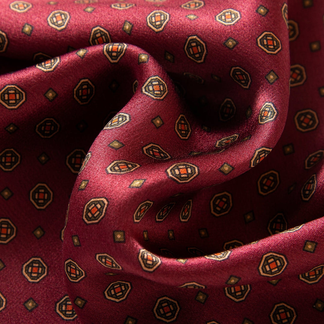 Close-up of the exquisite SusanSilk "Geometric Pattern Long Silk Scarf," showcasing a luxurious burgundy silk fabric adorned with a geometric pattern of small squares and octagons in muted colors, creating a textured, flowing appearance.