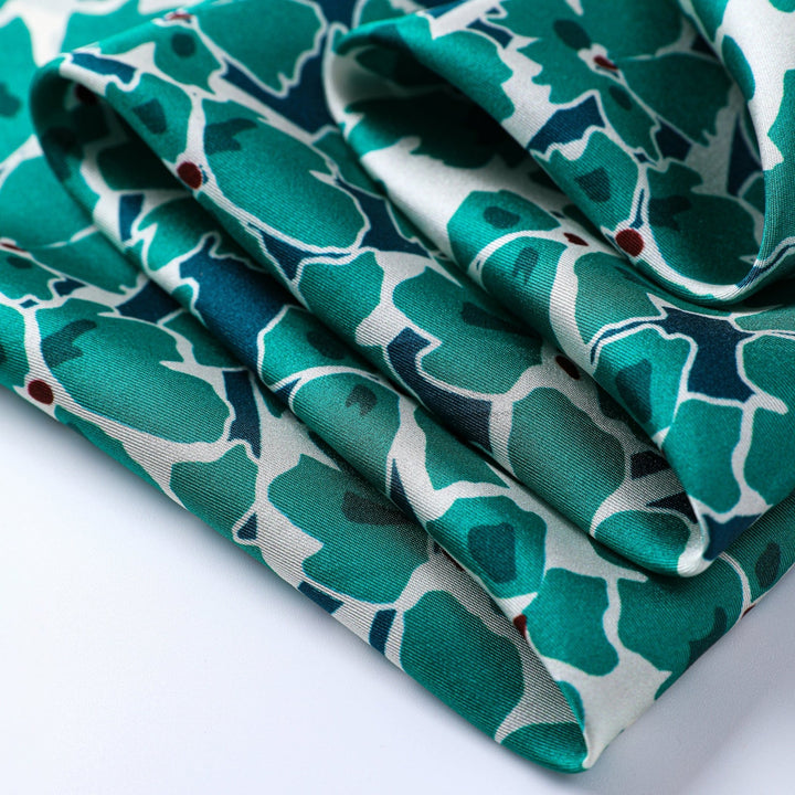 Close-up of the Green & Flourishing Flower Square Silk Scarf by SusanSilk, showcasing its folded silk fabric with a green and white abstract floral pattern and small red accents.