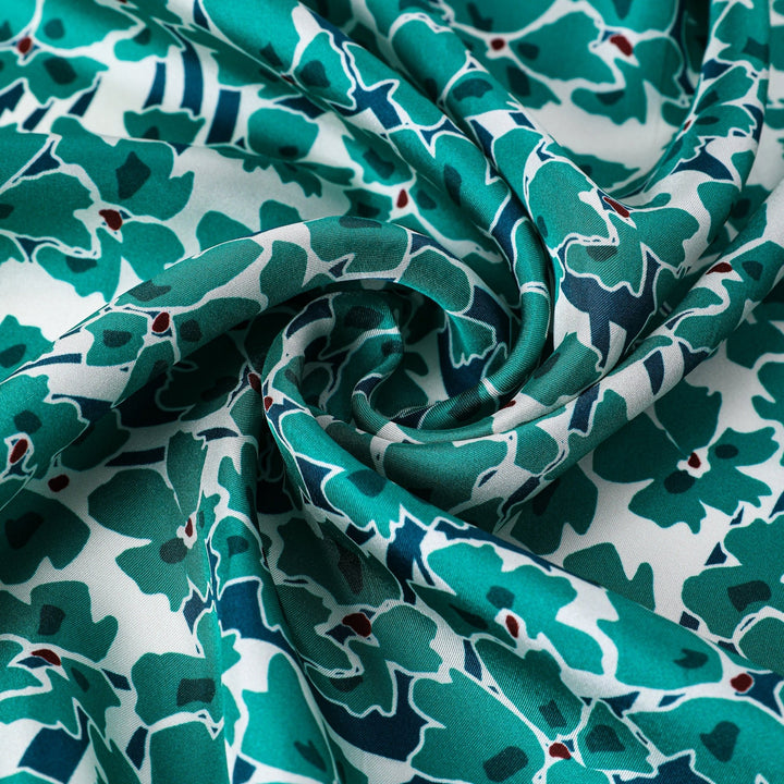 Close-up of a Green & Flourishing Flower Square Silk Scarf by SusanSilk, arranged in a spiral fold to showcase its intricate green and white floral pattern and luxurious texture.