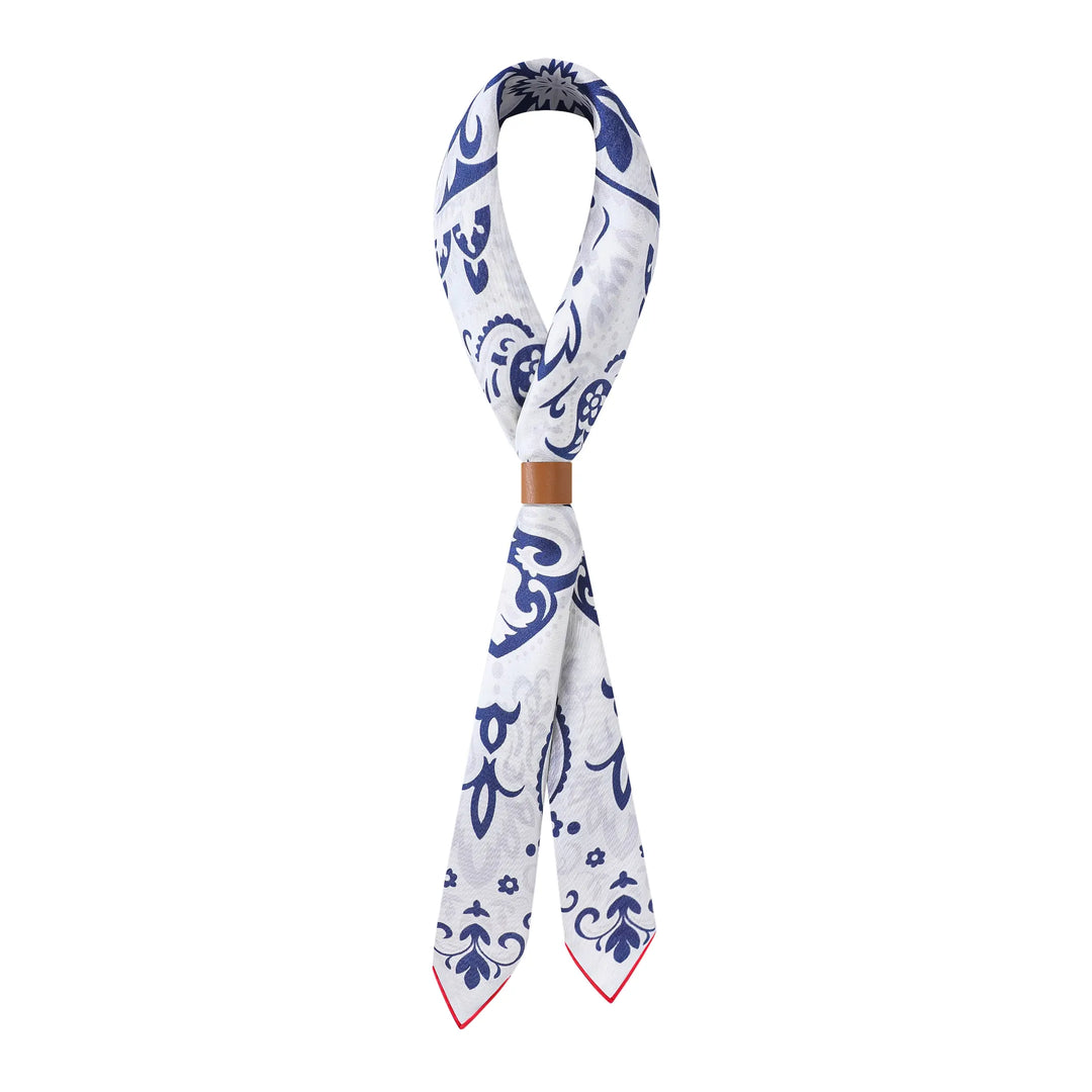 The Cashew Orchid Flower Square Silk Scarf from SusanSilk, featuring a white and blue pattern and a leather loop around the middle, is displayed against a white background.