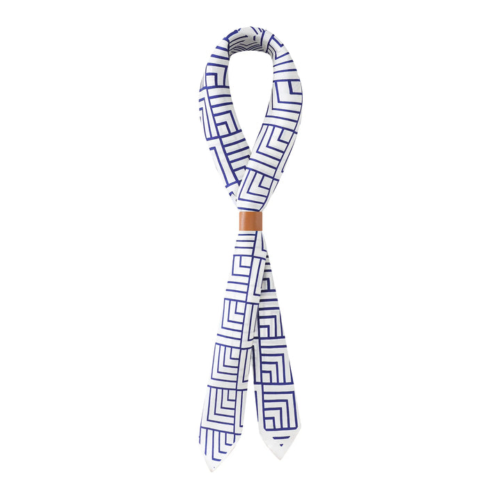 The SusanSilk Land Off Blue Square Silk Scarf, featuring a blue geometric pattern on white silk, is twisted into a knot with a brown accent near the center.