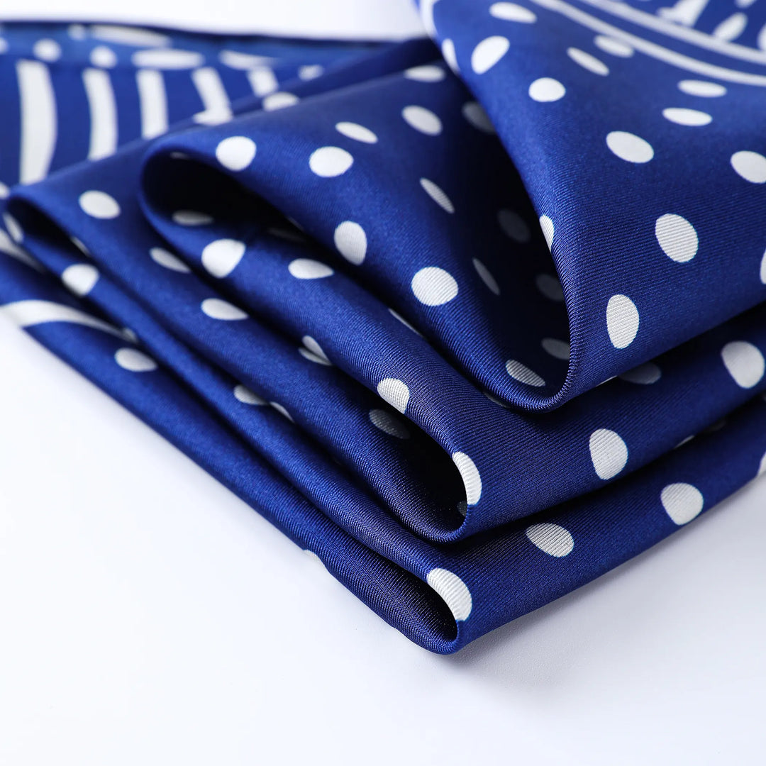 Close-up of the Flourishing Star Square Silk Scarf by SusanSilk, showcasing a folded navy blue silk fabric with white polka dots and stripes against a light background.