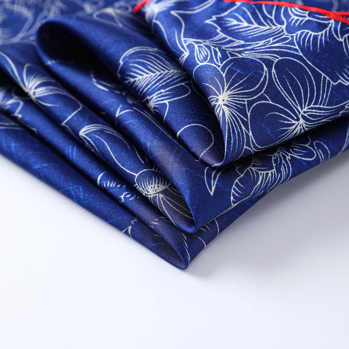 The SusanSilk Deep Blue Square Silk Scarf, featuring a white floral pattern, elegantly folded on a white surface.