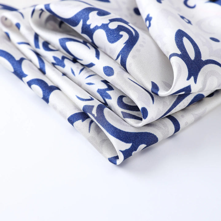 Folded SusanSilk's "Cashew Orchid Flower" square silk scarf, featuring an intricate blue floral pattern on a plain white background.