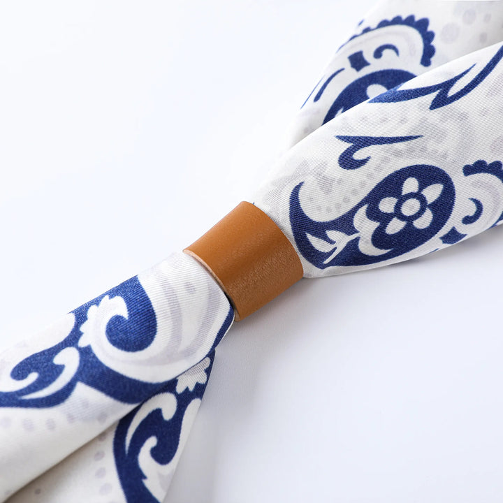 Close-up of the Cashew Orchid Flower Square Silk Scarf by SusanSilk, featuring a white and blue pattern, tied with a brown leather band in the middle.