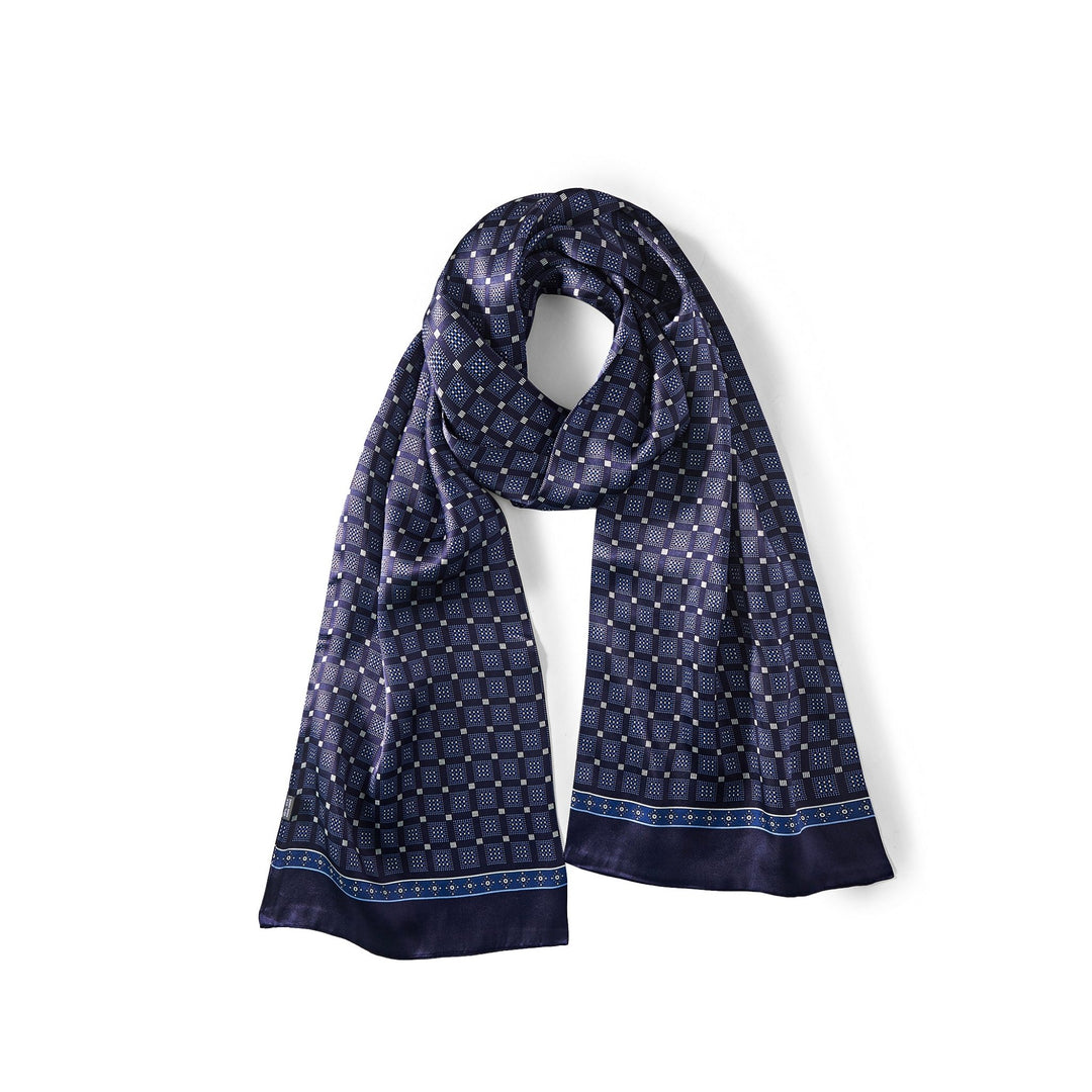 The SusanSilk Journey Grid Series Long Silk Scarf in dark blue, featuring a geometric pattern with small squares and dots, is laid flat with a loose loop at the top.