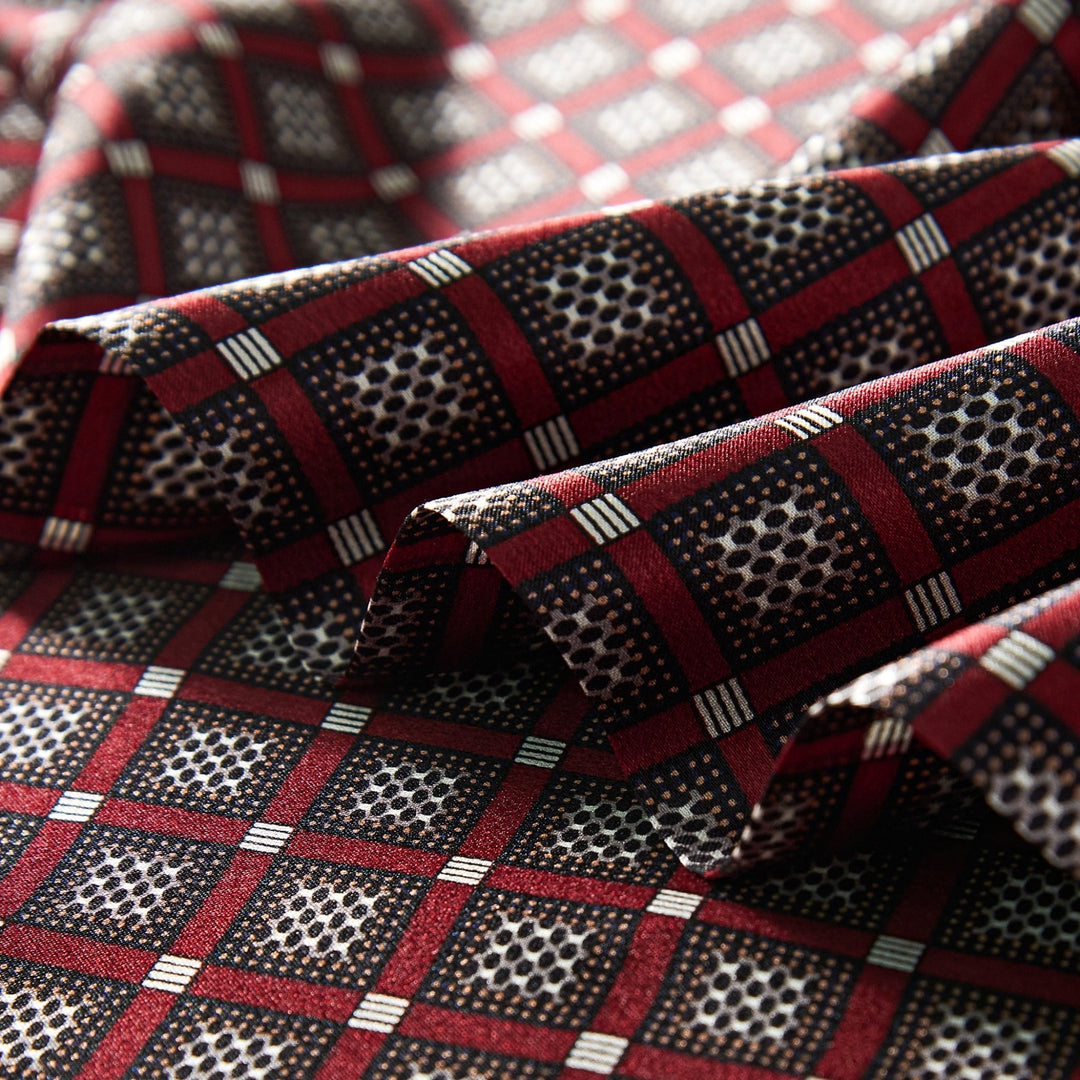 Close-up of the Journey Grid Series Long Silk Scarf by SusanSilk, featuring a red, black, and white geometric pattern with square and circular elements. The folded silk fabric shows visible creases.