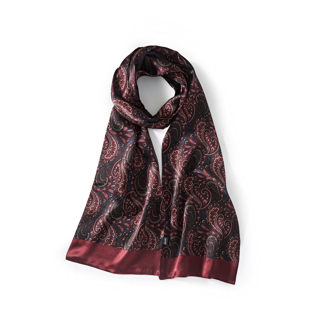 The SusanSilk Paisley Series Long Silk Scarf, featuring a black base adorned with a red paisley pattern and complemented by red satin trim, is neatly arranged against a white background to showcase its luxurious silk texture.