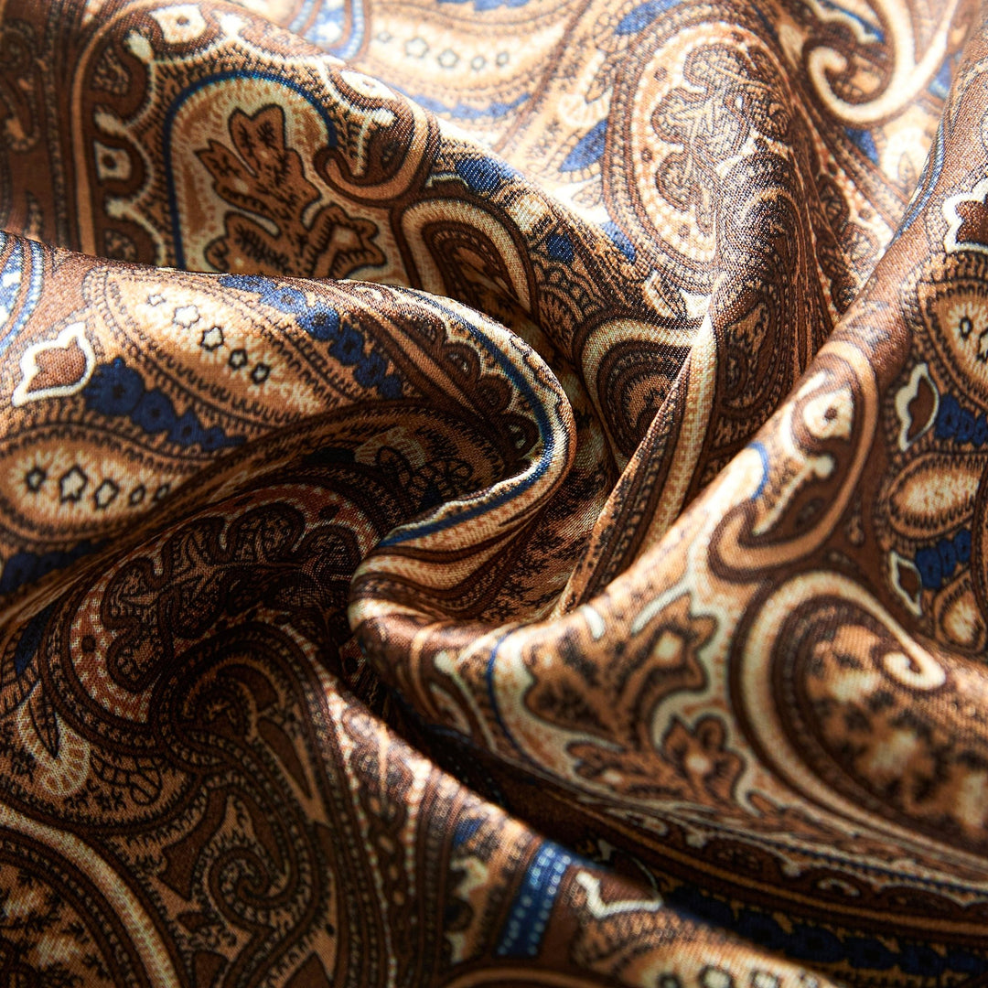 Close-up of the Paisley Series Long Silk Scarf by SusanSilk, showcasing its luxurious silk fabric adorned with an intricate paisley pattern in shades of brown, blue, and gold. The material appears to be smoothly draped and softly folded.