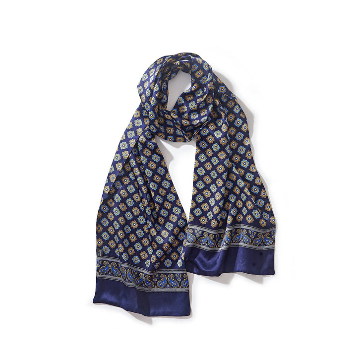 The Geometric Pattern Long Silk Scarf from SusanSilk features a blue silk fabric adorned with yellow and white geometric patterns, complemented by an intricate border design, making it a perfect choice for adding elegance to any outfit.