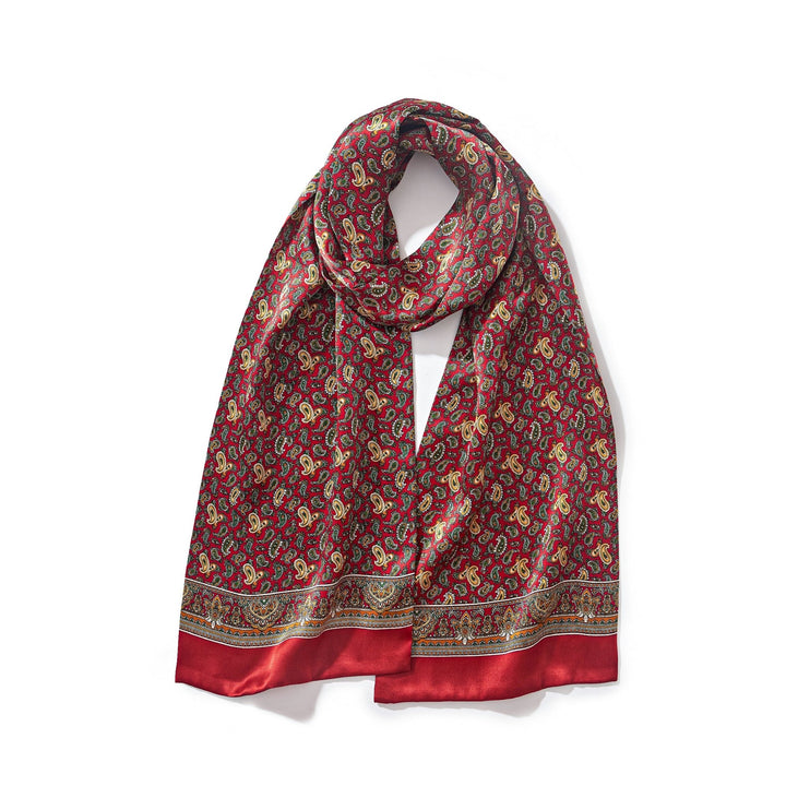 A Paisley Series Long Silk Scarf by SusanSilk, featuring intricate gold detailing against a red silk backdrop, is beautifully folded on a white background, showcasing the brand's exquisite craftsmanship.