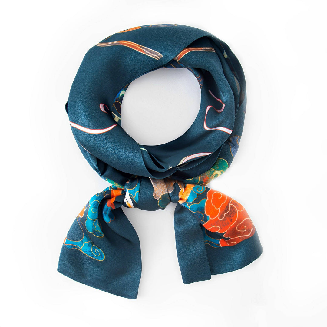 The Fairy Deer Long Mulberry Silk Scarf by SusanSilk, adorned with colorful patterns and designed in a stunning teal hue, is neatly tied in a loop with its ends gracefully hanging down.