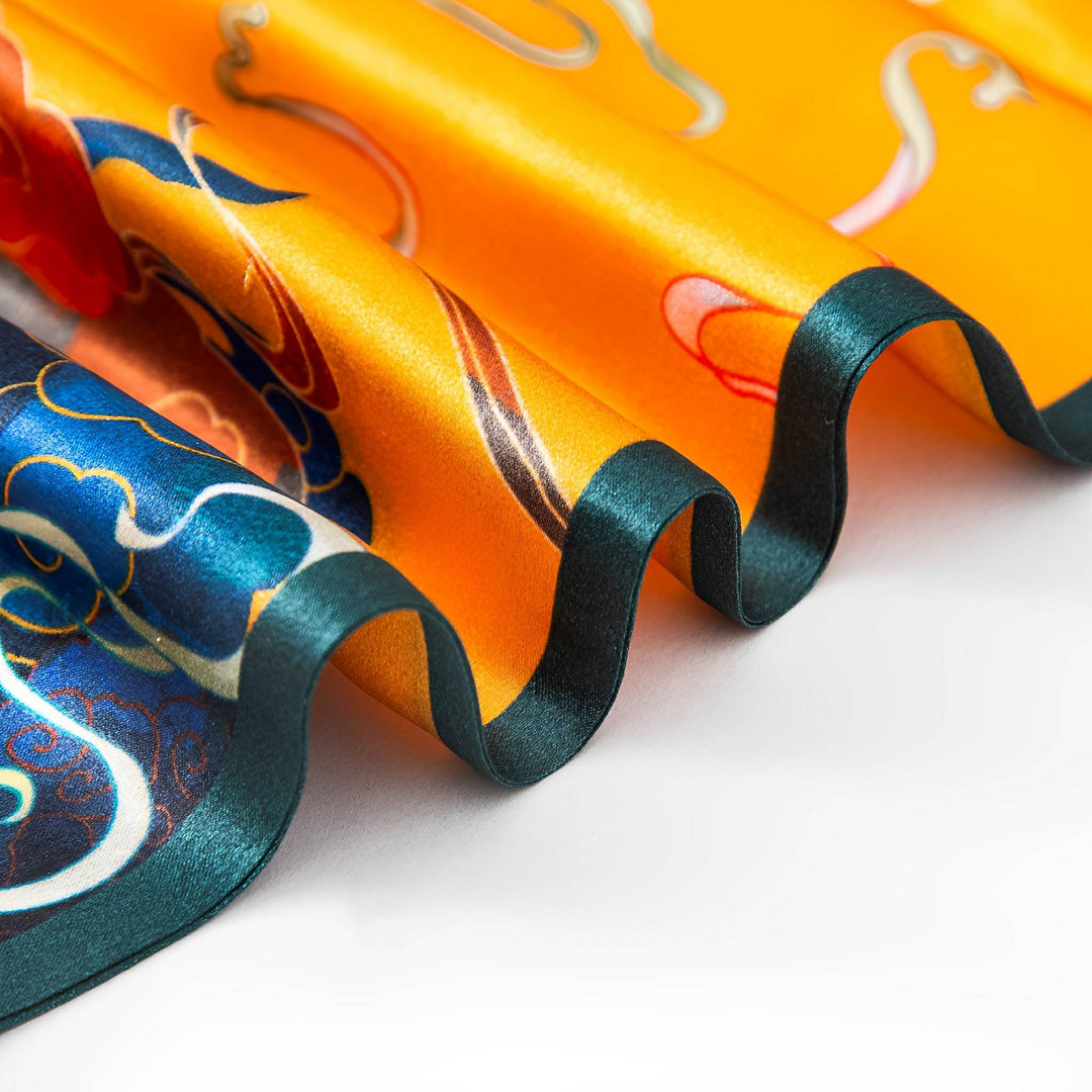 A close-up of the SusanSilk Fairy Deer Long Mulberry Silk Scarf, featuring vibrant orange, blue, and red patterns with a wavy, ruffled edge.