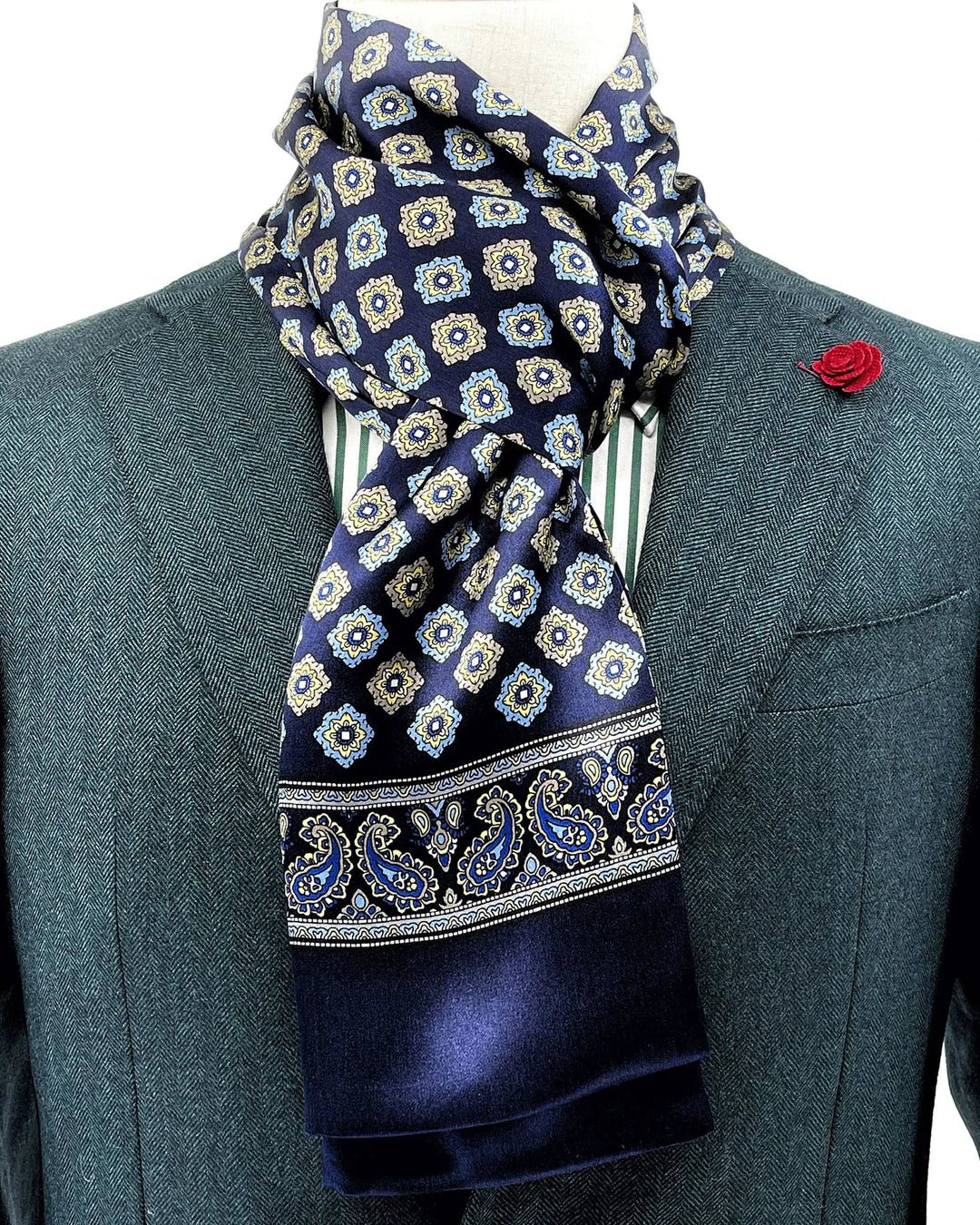 A person in a green suit, adorned with the SusanSilk Geometric Pattern Long Silk Scarf and a red lapel flower.