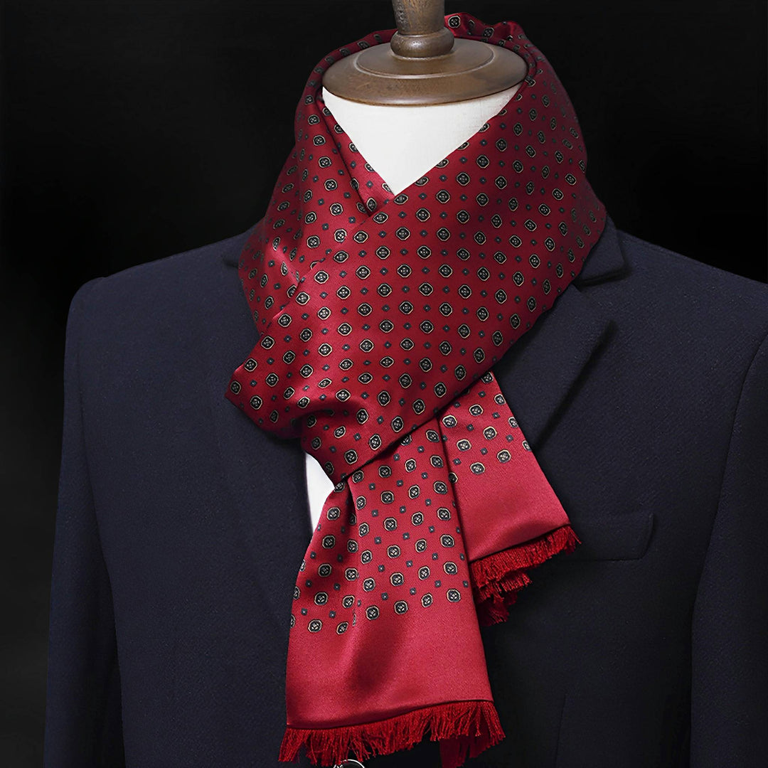 A mannequin dressed in a dark blazer is adorned with a deep red, geometric-patterned Geometric Series Long Silk Brushed Scarf from SusanSilk.