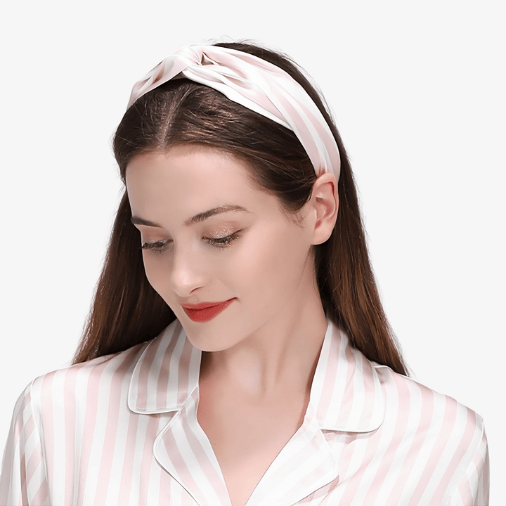 A woman with long brown hair wears a Stripe Criss Cross Silk Headband and matching silk pajama top from SusanSilk. She is looking down with a slight smile.