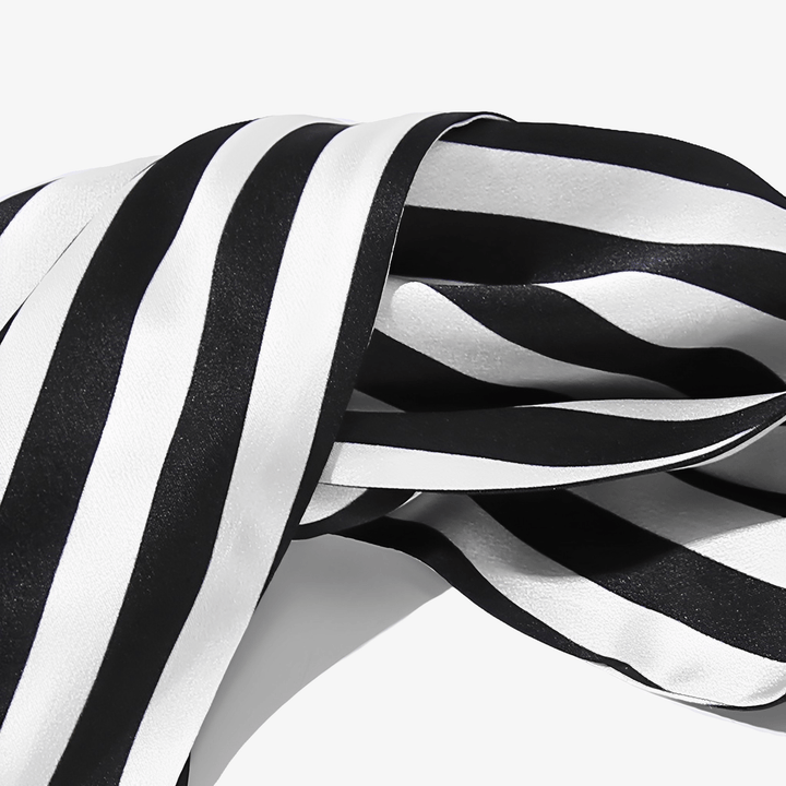 A close-up of the Stripe Criss Cross Silk Headband by SusanSilk shows its black and white striped fabric appearing smooth and glossy as it drapes and folds effortlessly.