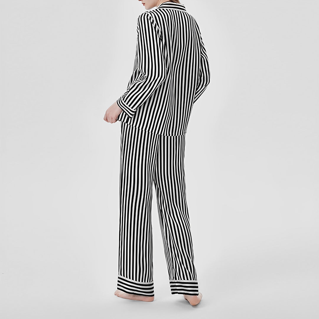 A person stands with their back turned, wearing the SusanSilk 19 Momme Chic Stripe Silk Pajamas Set against a plain backdrop.