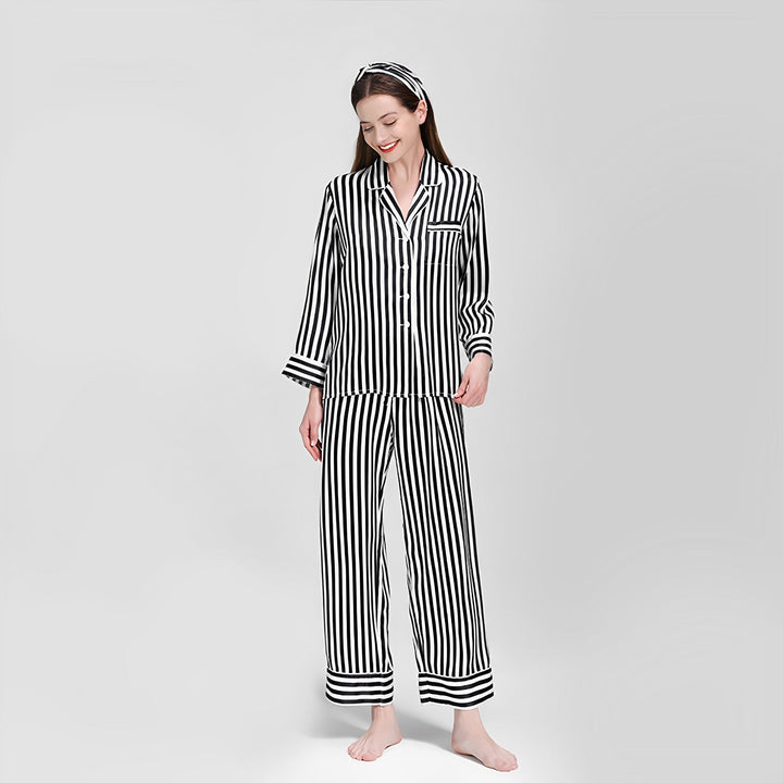 A woman is standing and smiling while wearing the 19 Momme Chic Stripe Silk Pajamas Set by SusanSilk, complete with a matching headband, against a plain background.