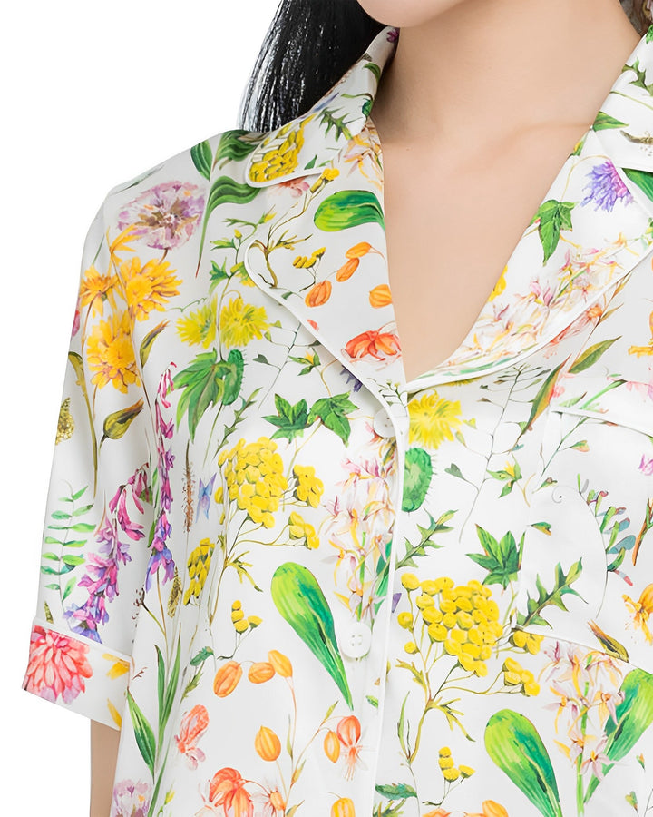 Close-up of a person wearing the Floral Short Silk Pajamas Set from SusanSilk, featuring a colorful floral pattern with various flowers and green leaves. Only the torso and part of the head are visible.