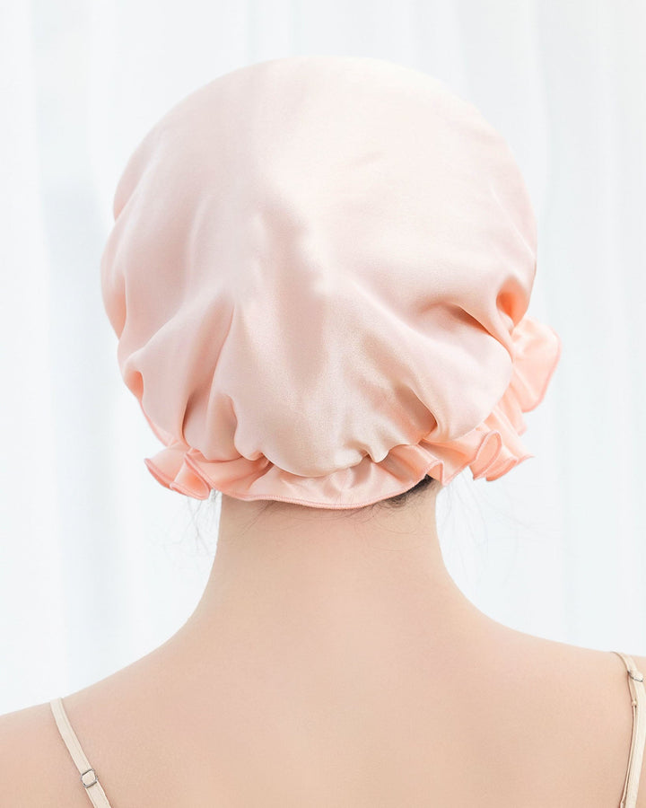 A person with their back to the camera wearing a pale pink Flounced Silk Bonnet For Sleeping by SusanSilk.