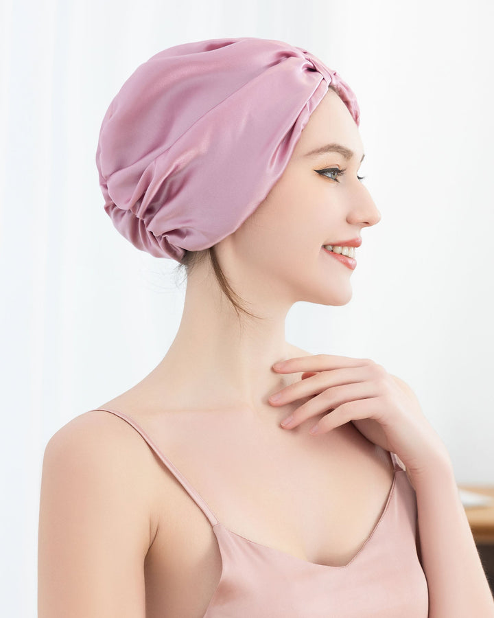 A woman in a sleeveless top is smiling and wearing a pink Elegant Pleated Silk Bonnet For Sleeping from SusanSilk over her hair.