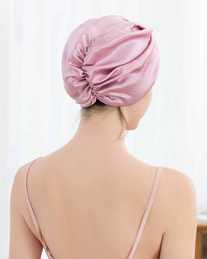 Person wearing an Elegant Pleated Silk Bonnet For Sleeping by SusanSilk in light pink, seen from behind, with shoulders and upper back exposed.