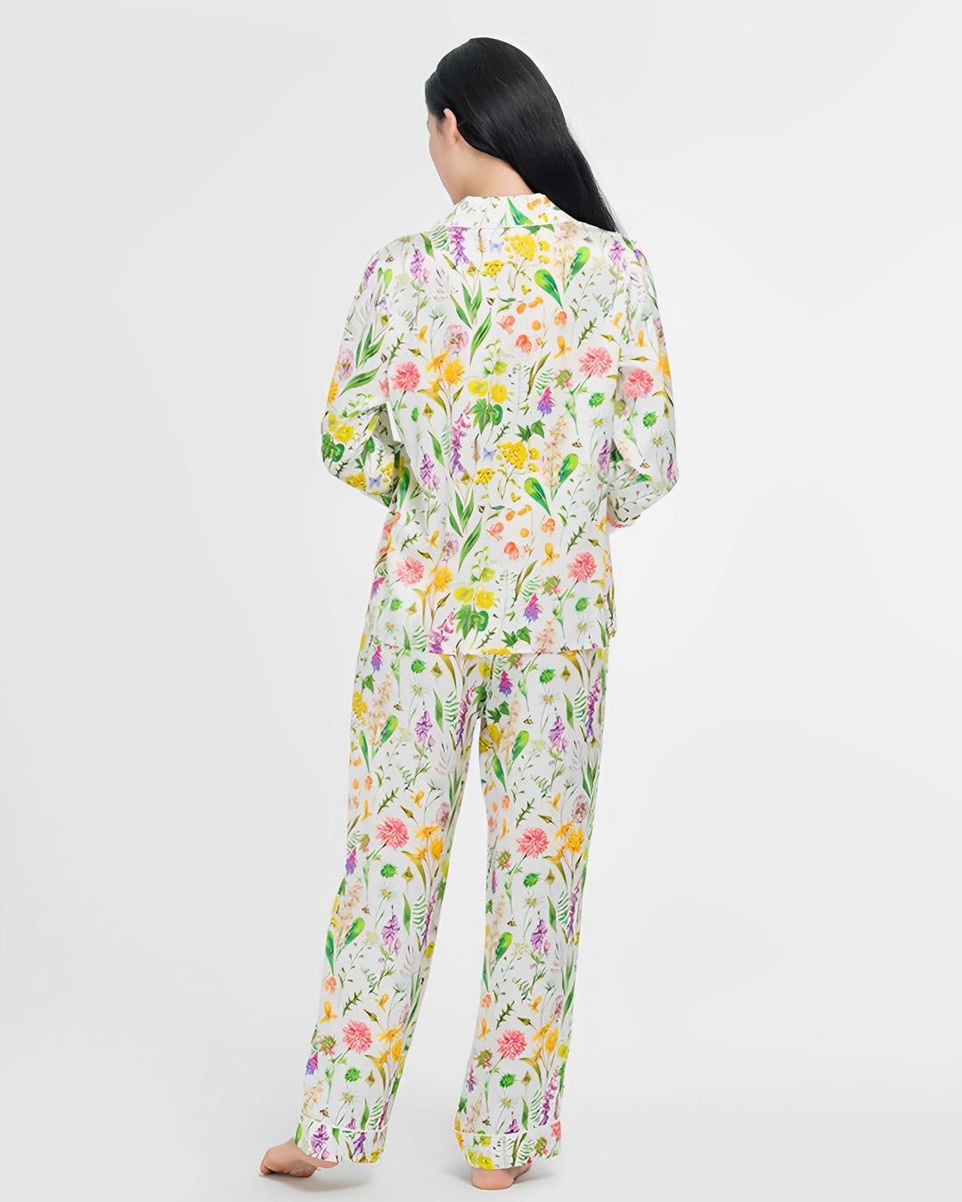 A person with long dark hair is standing in a SusanSilk 19 Momme Floral Silk Pajamas Set, facing away from the camera. The background is plain white.