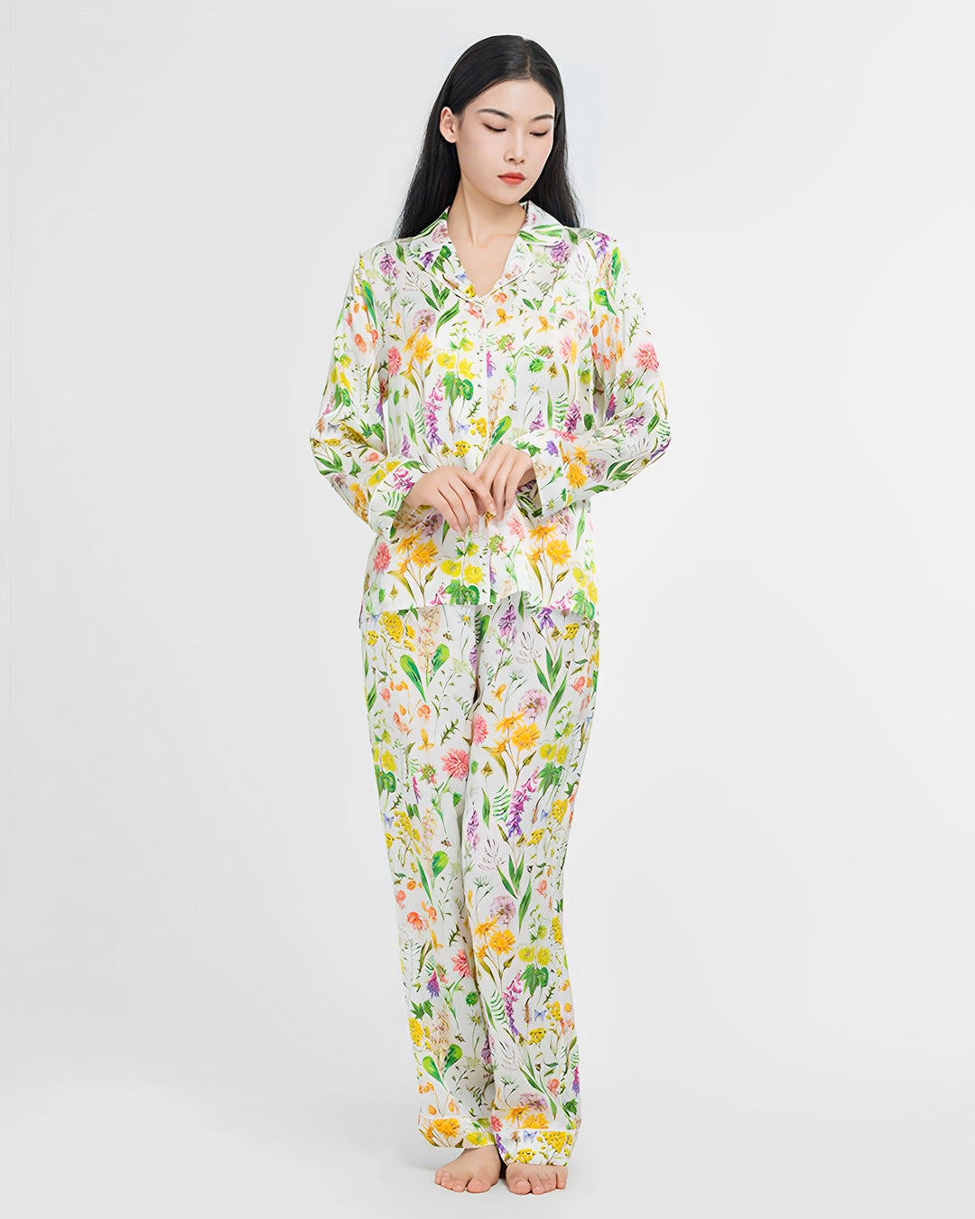 A woman with long black hair stands barefoot, wearing a matching 19 Momme Floral Silk Pajama Set by SusanSilk.