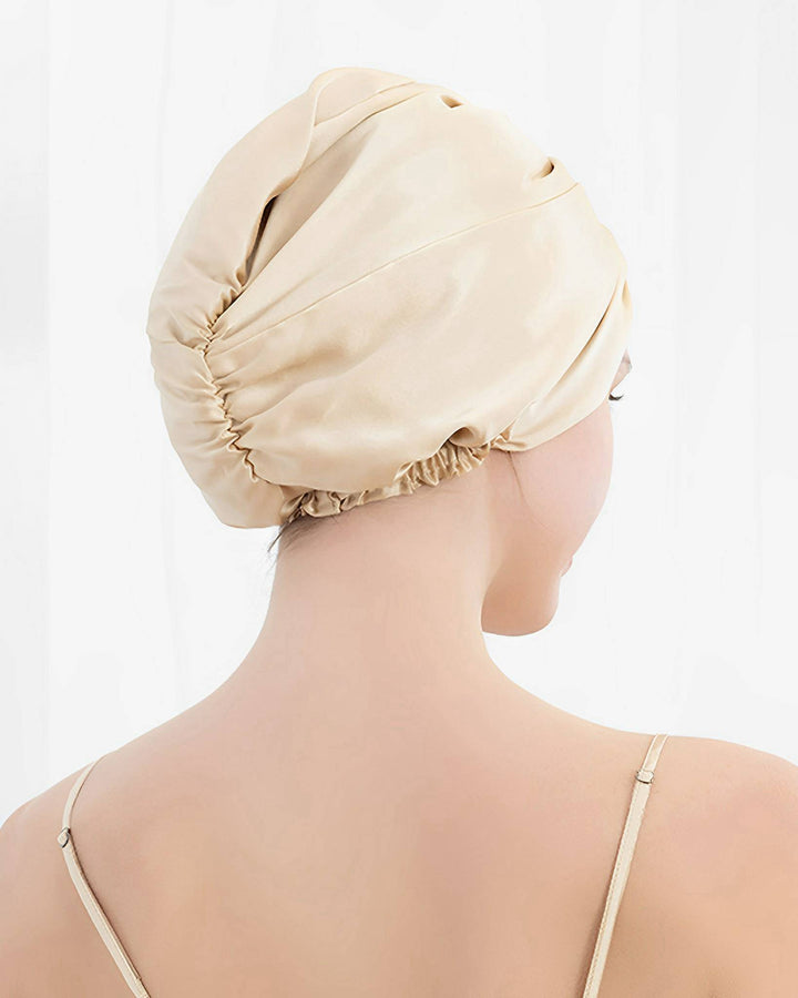 A person adorned in a beige SusanSilk Luxury Turban Silk Sleep Cap, shown from the back, with the silk cap fully covering their hair.