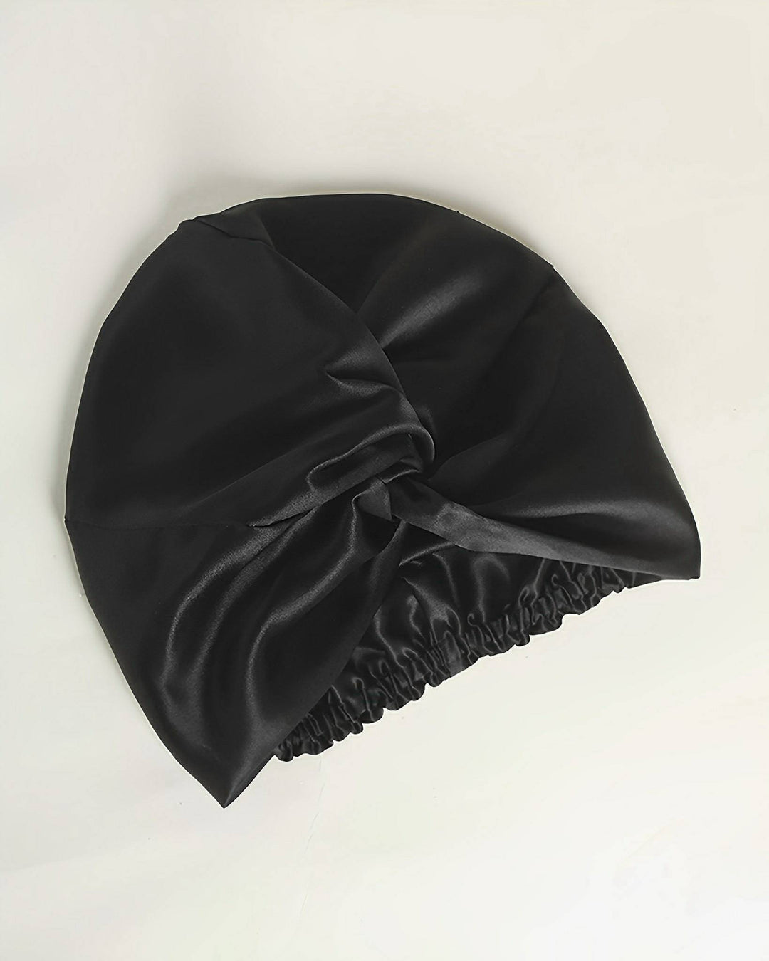 SusanSilk's Luxury Turban Silk Sleep Cap is a black satin bonnet meticulously crafted from luxurious silk, featuring an elegant knot design on top and an elastic band at the opening.