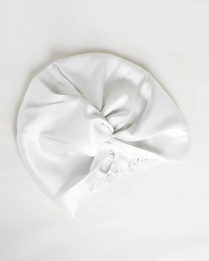 The Luxury Turban Silk Sleep Cap by SusanSilk features a gathered elastic band and a twisted knot design at the top, all crafted from luxurious white satin.