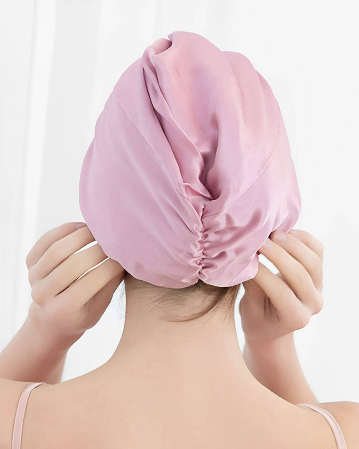 A person with their back to the camera adjusts a Luxury Turban Silk Sleep Cap by SusanSilk on their head.