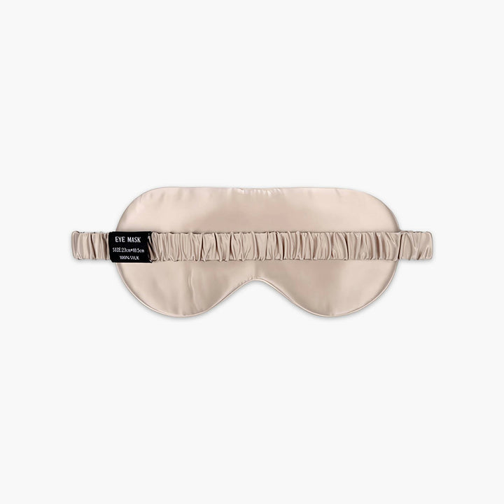 The Elegant Silk Eye Mask - Colorful Sailboat by SusanSilk is a beige satin eye mask crafted from luxurious silk, featuring an elastic band and a black label on the side displaying text.