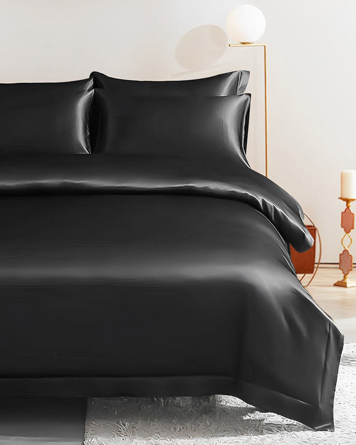 A neatly made bed adorned with the SusanSilk 19 Momme Seamless Silk Duvet Cover - Flange Border in black satin is shown. The room features minimalistic decor, including a lamp and a candle holder in the background, creating an elegant SusanSilk ambiance.