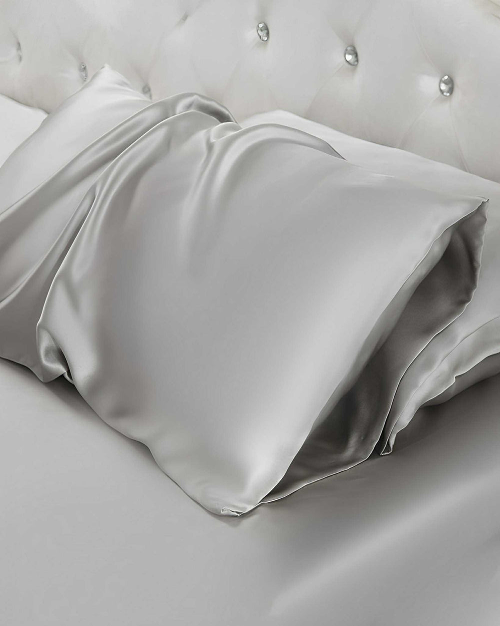 Two 19 Momme Silk Pillowcase Envelopes in silver satin lay upon a tufted white headboard bed, crafted from luxurious SusanSilk.