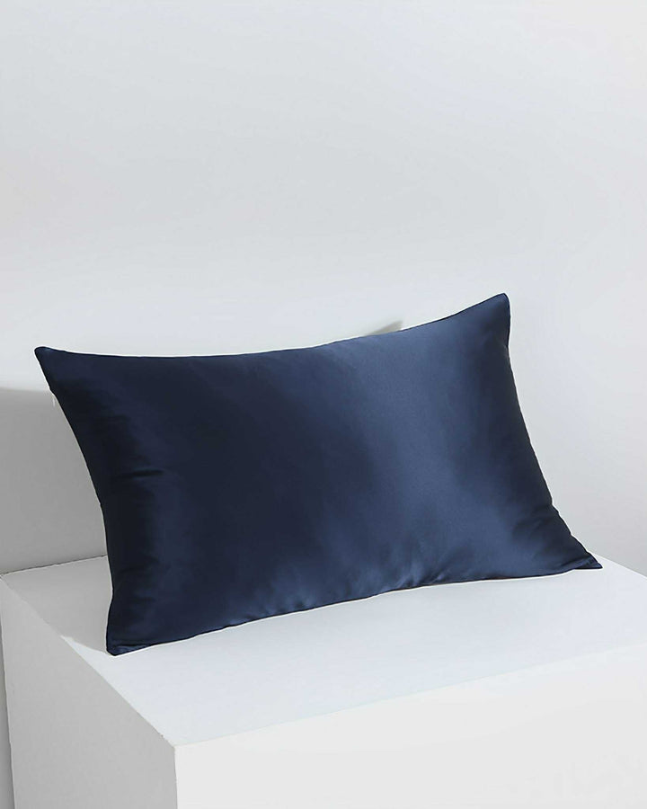 A 19 Momme Silk Pillowcase Zipper in navy blue from SusanSilk, resembling luxurious satin, is placed on a white surface against a white background.