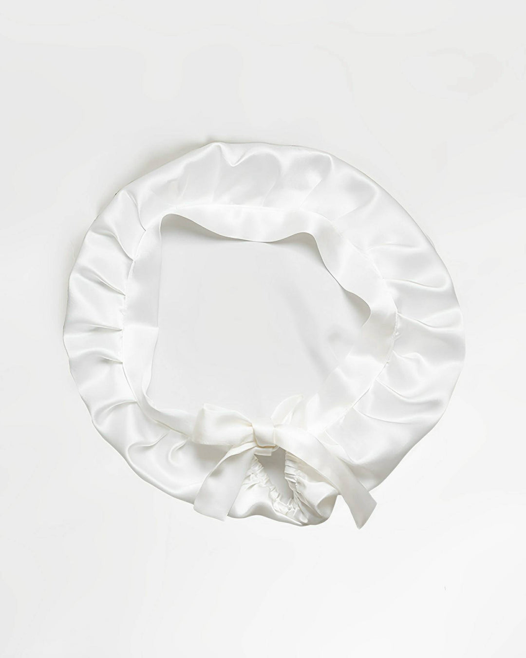 A white Chic Silk Bonnet For Sleeping with Ribbons by SusanSilk, featuring a ruffled edge and a bow at the front, is displayed against a plain background, highlighting its elegance.