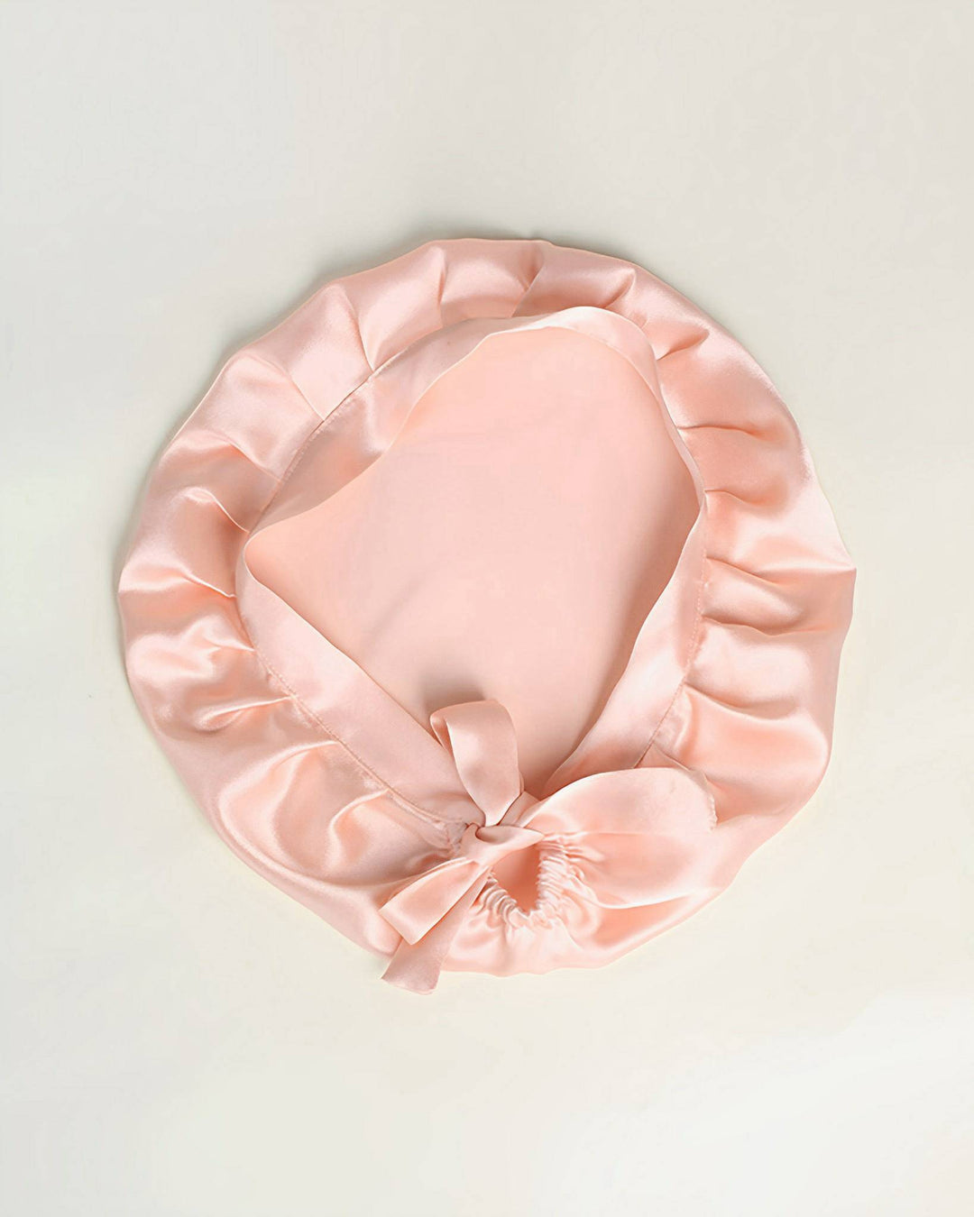 A Chic Silk Bonnet For Sleeping with Ribbons by SusanSilk, available in pink satin and featuring a ruffled edge with a ribbon tied at the front.