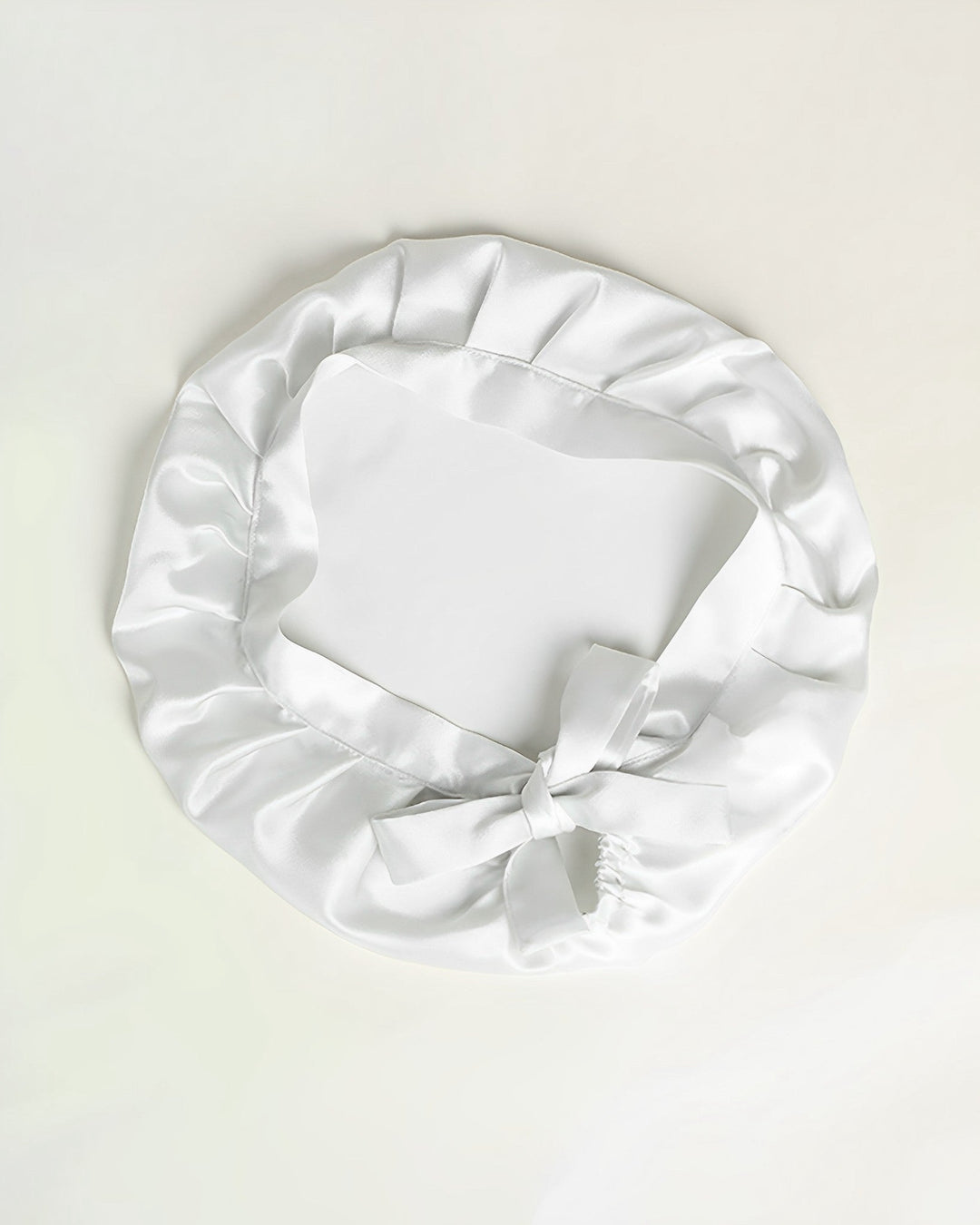 A Chic Silk Bonnet For Sleeping with Ribbons from SusanSilk, featuring a ruffled edge and a bow at the front, is displayed on a plain white background.