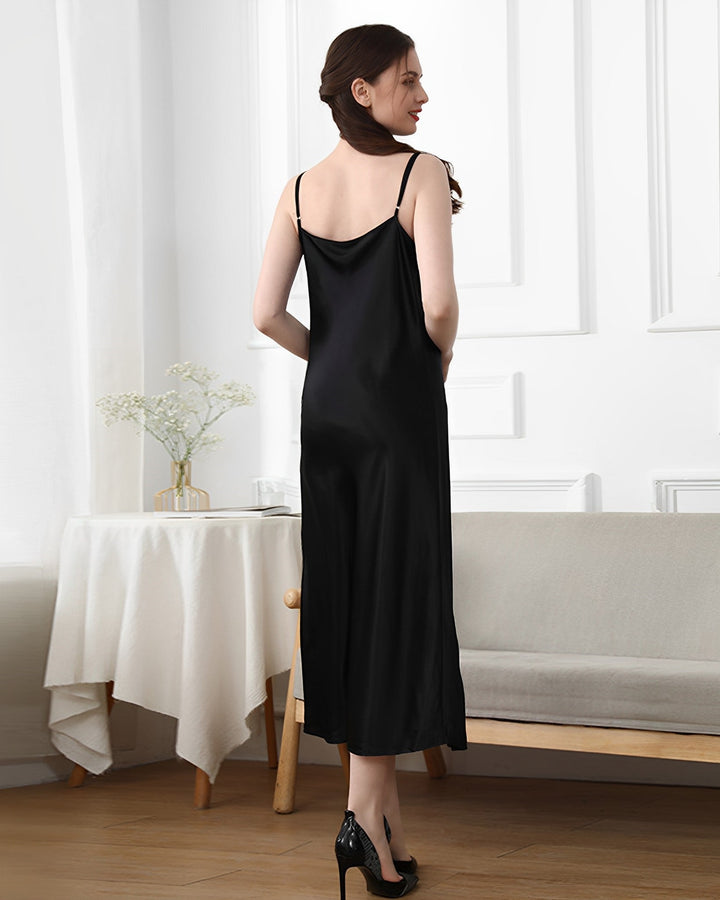 A woman wearing the 19 Momme Silk Sling Dress for Women by SusanSilk and high heels stands by a white table and a beige sofa, facing away from the camera in a well-lit room.